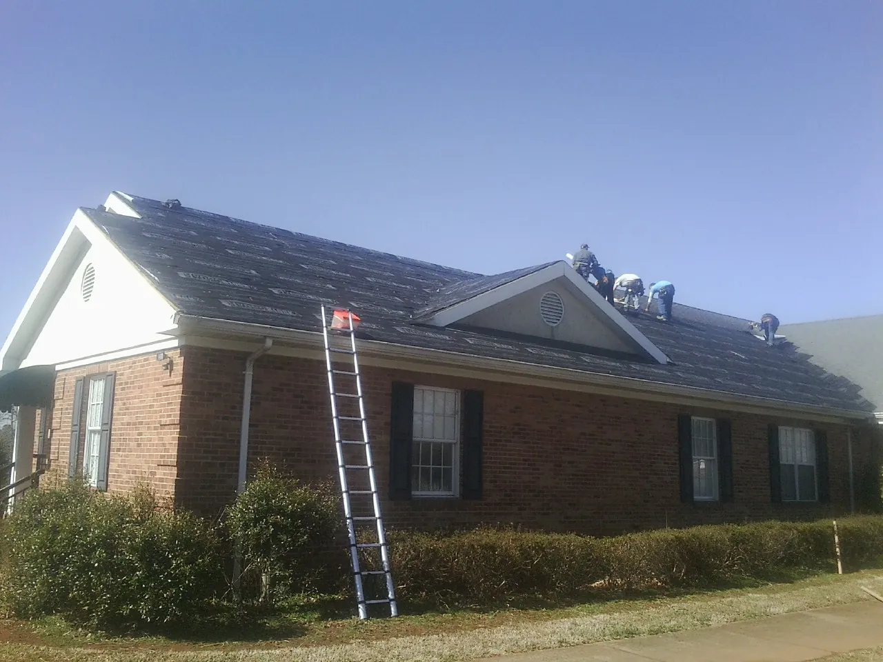 Crew tearing shingles off a brick ranch roof with a ladder set — Metal Roof Repair work by our crew in Alpha
