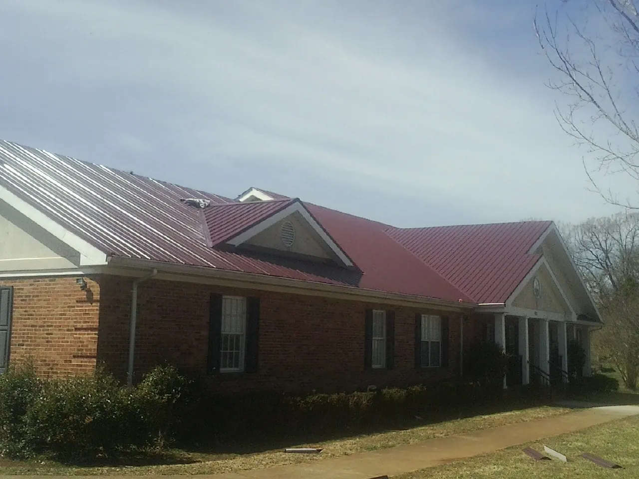 Red metal roof with gabled entries on a long brick building, from a Hail Damage Roof Repair job in Alpha