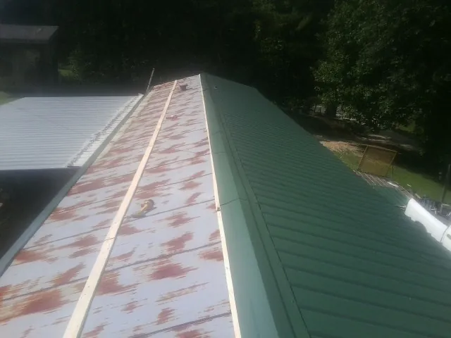 Old rusted panels beside newly installed green metal roofing — Wind Damage Roof Repair by Roofing Brothers in Alpha